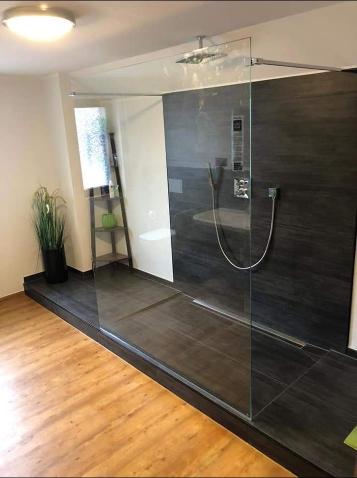 Duschbad mit dunklen Wandfliesen, Glasabtrennung und Holzoptikboden