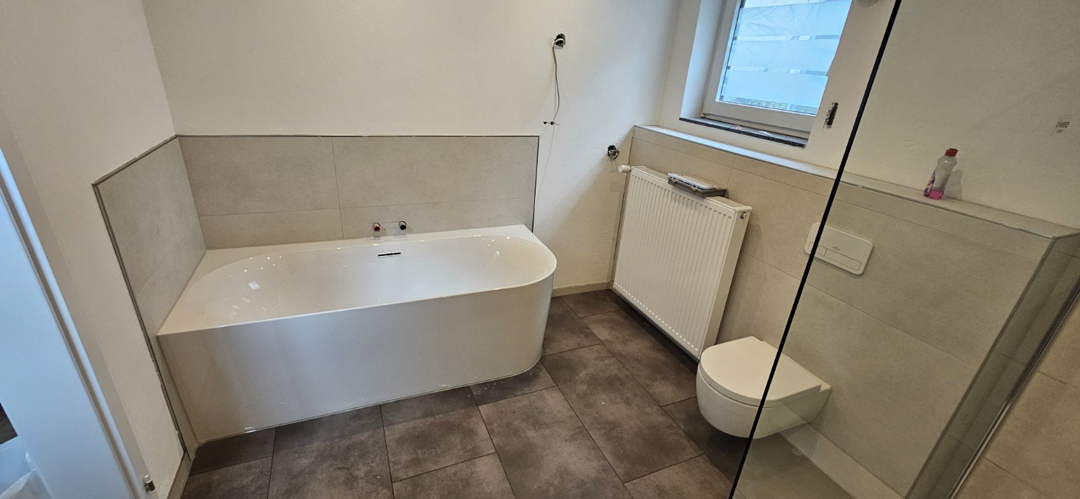 Weitere Ansicht des Badezimmers mit Badewanne und großformatigen Bodenfliesen
